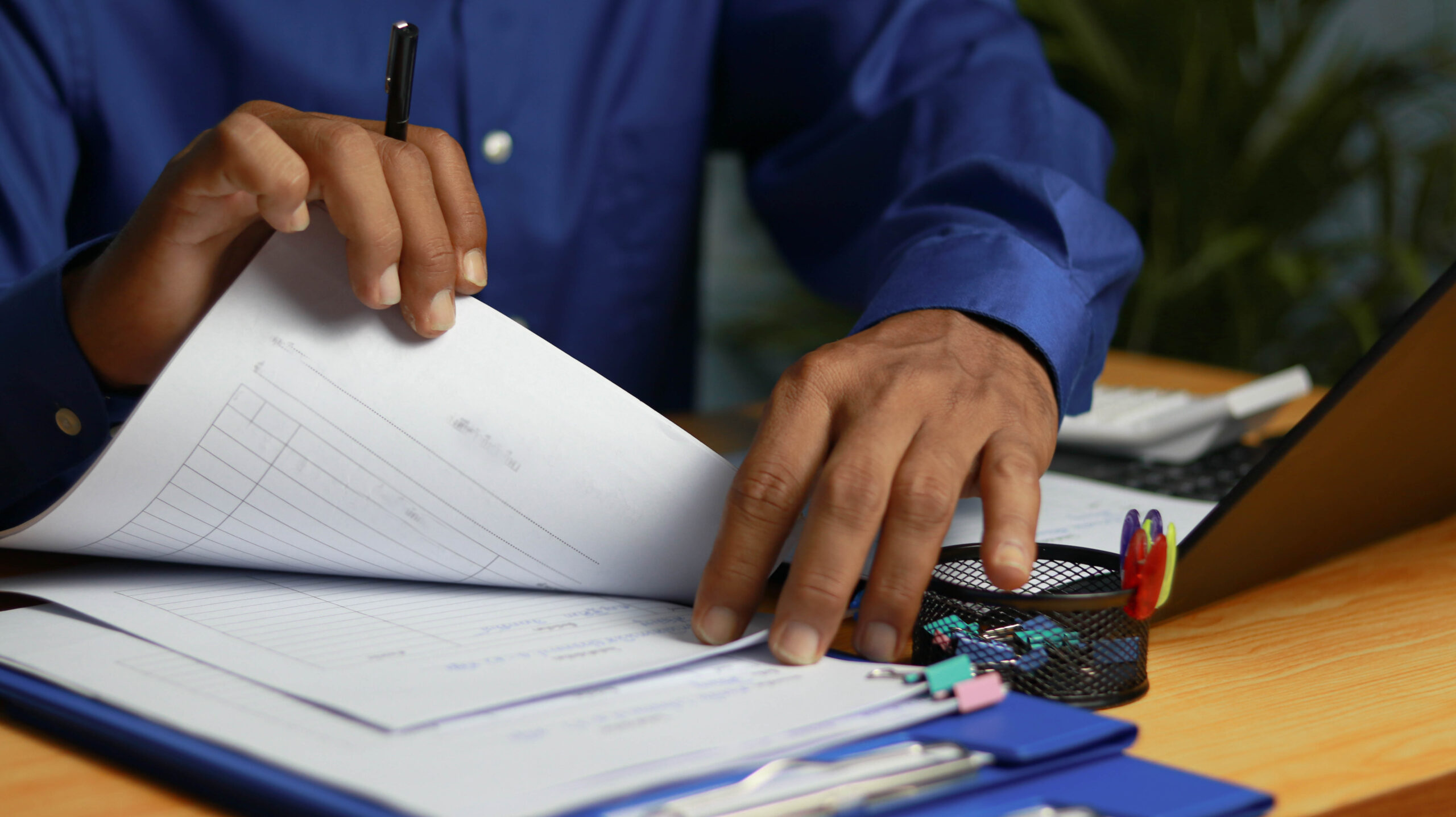 Business professional reviewing and organizing paperwork on a clipboard at a modern office desk with a laptop and office supplies, representing document management, administra, and corporate workflow.